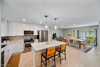 Kitchen with appliances with stainless steel finishes, backsplash, hanging light fixtures, a kitchen island, and white cabinetry
