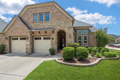 This is a single-family home featuring a brick and stone facade, dual garage doors, and manicured landscaping with a curved stone lined flower bed. The home has a welcoming entrance with an arched entryway and a transom window above for natural light.