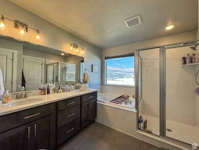 Bathroom with a textured ceiling, a shower stall, double vanity, a bath, and tile patterned flooring