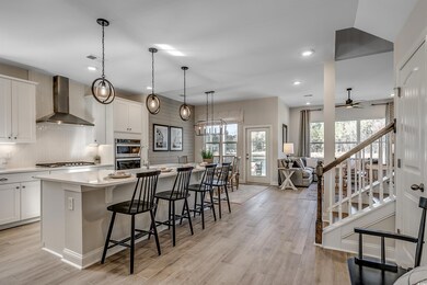 Kitchen with tasteful backsplash, appliances with stainless steel finishes, a kitchen island with sink, light wood-type flooring, and wall chimney range hood