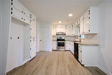 Kitchen with stainless steel range with electric cooktop, under cabinet range hood, black dishwasher, a sink, and light wood finished floors