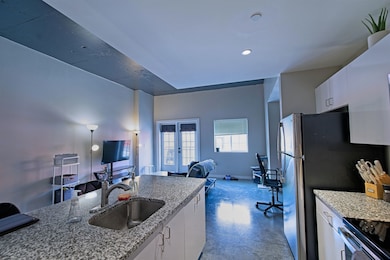 Kitchen featuring a sink, open floor plan, white cabinets, french doors, and light stone counters