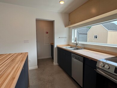 Kitchen featuring wood counters, finished concrete floors, appliances with stainless steel finishes, dark cabinetry, and electric panel