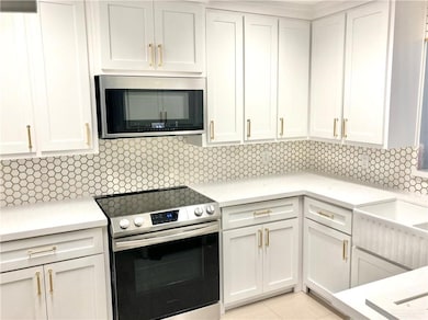 Kitchen with appliances with stainless steel finishes, light countertops, decorative backsplash, and white cabinetry