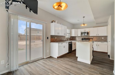 Kitchen with hanging light fixtures, a kitchen island, dark wood finished floors, tasteful backsplash, and white cabinets