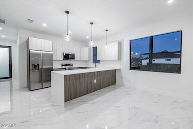 Kitchen featuring recessed lighting, stainless steel appliances, modern cabinets, light marble finish flooring, and a peninsula