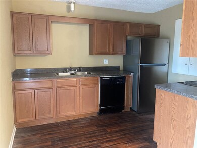 Kitchen featuring dark countertops, black dishwasher, freestanding refrigerator, dark wood-type flooring, and brown cabinets