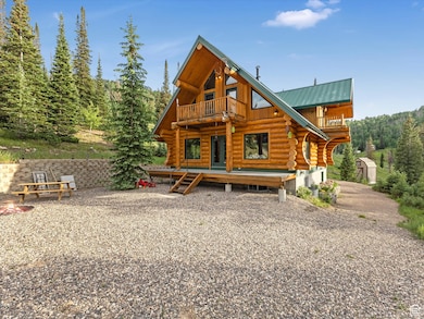 Rear view of property with log exterior, a balcony, a wooden deck, a metal roof, and a forest view
