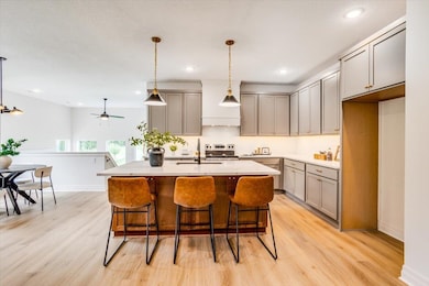 Kitchen featuring gray cabinetry, decorative light fixtures, a kitchen breakfast bar, a center island with sink, and light wood finished floors