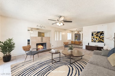 Living room featuring light tile patterned flooring, a textured ceiling, a fireplace, and a ceiling fan