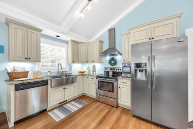 Kitchen featuring cream cabinets, appliances with stainless steel finishes, wall chimney range hood, light wood-type flooring, and light stone counters