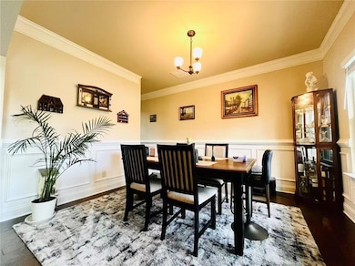 Dining room featuring ornamental molding, a chandelier, a decorative wall, dark wood finished floors, and wainscoting
