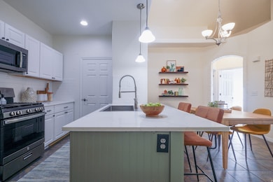Kitchen featuring appliances with stainless steel finishes, white cabinets, a kitchen bar, backsplash, and pendant lighting