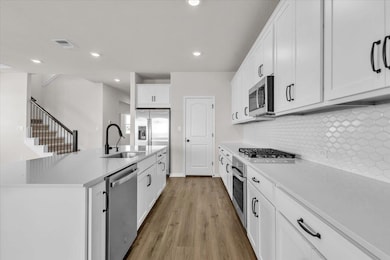 Kitchen with white cabinetry, appliances with stainless steel finishes, an island with sink, light wood-style floors, and recessed lighting