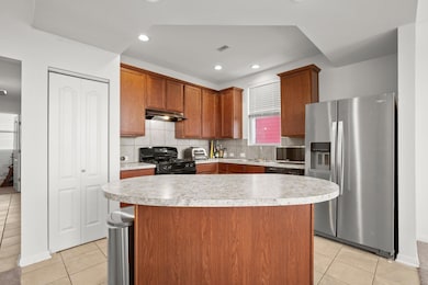 Kitchen featuring stainless steel appliances, light tile patterned flooring, light countertops, backsplash, and brown cabinetry