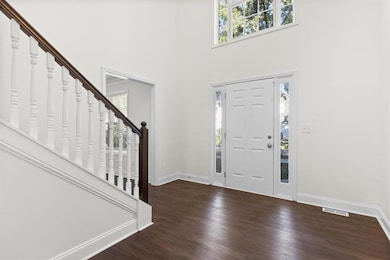 Foyer entrance with healthy amount of natural light, dark wood-style floors, stairs, and a towering ceiling
