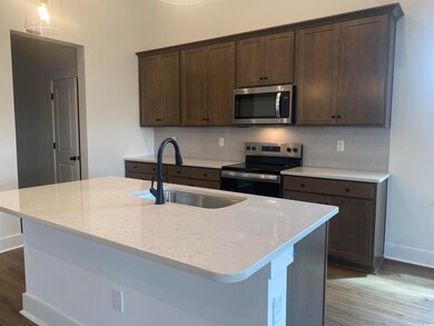 Kitchen featuring appliances with stainless steel finishes, a sink, baseboards, wood finished floors, and light stone counters