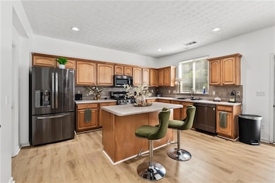 Kitchen with stainless steel appliances, light wood-style floors, light countertops, a center island, and a kitchen bar