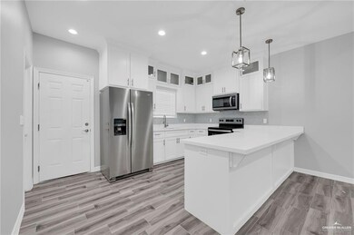Kitchen featuring stainless steel appliances, a peninsula, glass insert cabinets, light countertops, and white cabinetry