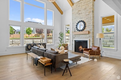 Living room featuring beamed ceiling, a stone fireplace, wood-type flooring, and high vaulted ceiling