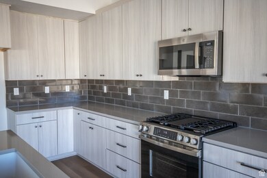 Kitchen with stainless steel appliances, backsplash, light stone counters, and modern cabinets