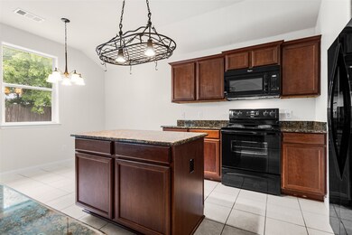 Kitchen featuring black appliances, light tile patterned flooring, vaulted ceiling, a center island, and pendant lighting