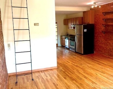 Kitchen featuring stainless steel appliances, brick wall, light wood-type flooring, and brown cabinetry