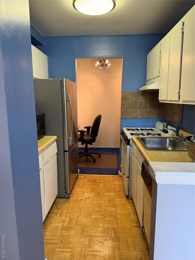 Kitchen featuring white cabinets, appliances with stainless steel finishes, light countertops, range hood, and decorative backsplash
