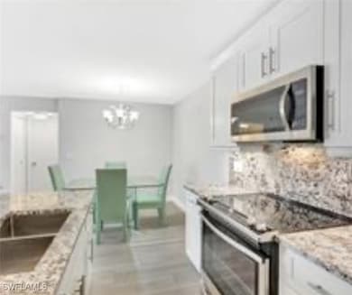 Kitchen with appliances with stainless steel finishes, white cabinets, light stone countertops, and tasteful backsplash