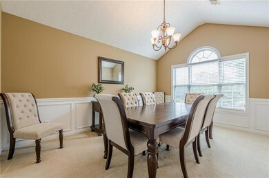 Dining area featuring a chandelier, light colored carpet, a wainscoted wall, vaulted ceiling, and a decorative wall