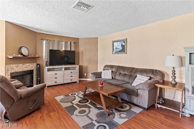 Living room with a textured ceiling, wood finished floors, and a fireplace