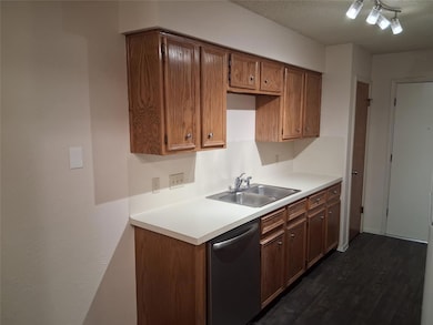 Kitchen with stainless steel dishwasher, dark wood-type flooring, light countertops, and brown cabinetry