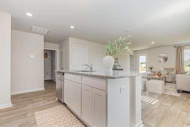 Kitchen featuring light stone counters, recessed lighting, light wood-type flooring, white cabinetry, and an island with sink