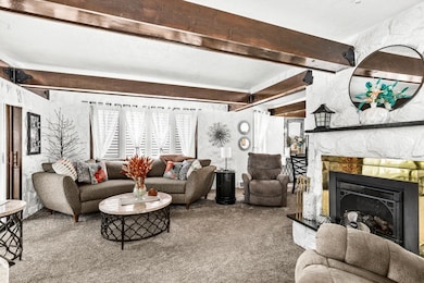 Living room with beam ceiling, carpet, and a stone fireplace