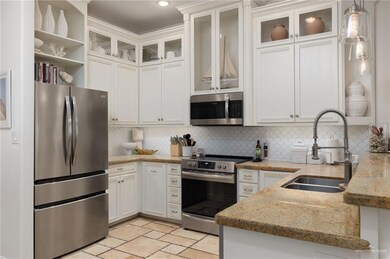 Kitchen featuring appliances with stainless steel finishes, decorative backsplash, white cabinetry, light stone countertops, and pendant lighting