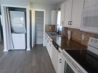 Kitchen with white appliances, backsplash, white cabinets, and dark stone counters