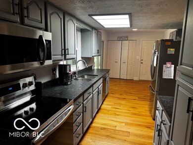 kitchen with stainless steel appliances, light wood-style floors, a textured ceiling, and dark stone counters