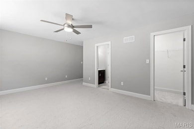 Unfurnished bedroom featuring light colored carpet, ceiling fan, a spacious closet, connected bathroom, and a closet