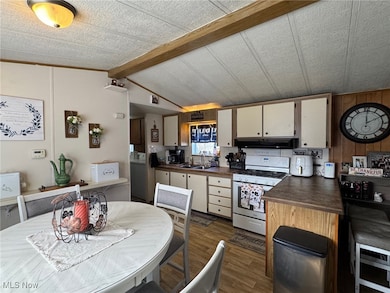 Kitchen with white gas range, dark wood-style floors, under cabinet range hood, dark countertops, and white cabinetry
