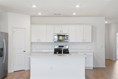 Kitchen with white cabinets, appliances with stainless steel finishes, light wood-style flooring, an island with sink, and recessed lighting