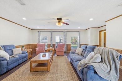 Living room with wood walls, wood finished floors, a wainscoted wall, crown molding, and a textured ceiling
