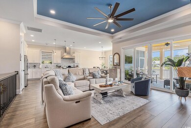 Living room with a ceiling fan, a tray ceiling, wood finished floors, a chandelier, and crown molding