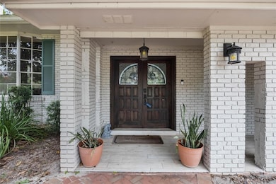 This photo shows the front entrance of a home with a white-painted brick exterior. The entryway features a pair of dark wooden double doors with decorative arched glass inserts. A hanging lantern-style light fixture is centered above the doorway, and matching wall-mounted lights are installed on either side of the entrance. Two terracotta pots with snake plants (Sansevieria) are positioned symmetrically on either side of the door. A beige 