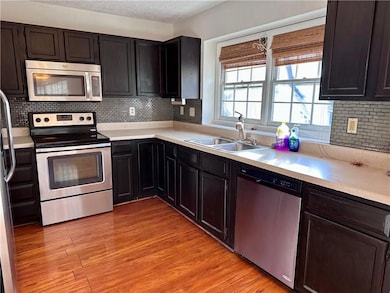 Kitchen with stainless steel appliances, a textured ceiling, light countertops, light wood-type flooring, and a sink