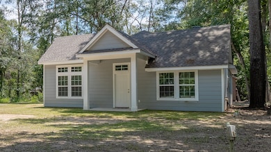 The home has a welcoming front entrance and multiple windows for natural light. A serene natural setting with mature trees.