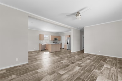 Unfurnished living room featuring ornamental molding, light wood-type flooring, and a ceiling fan