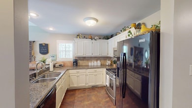 Kitchen with a sink, black appliances, light stone counters, and white cabinetry