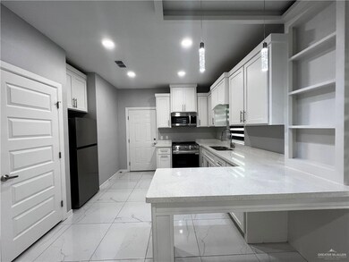 Kitchen featuring a peninsula, open shelves, light marble finish floors, stainless steel appliances, and white cabinetry