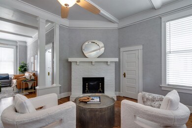 Living area with wood finished floors, beam ceiling, crown molding, a ceiling fan, and decorative columns