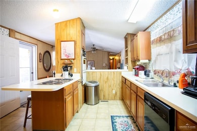 Kitchen featuring a peninsula, light countertops, a kitchen breakfast bar, black dishwasher, and a textured ceiling